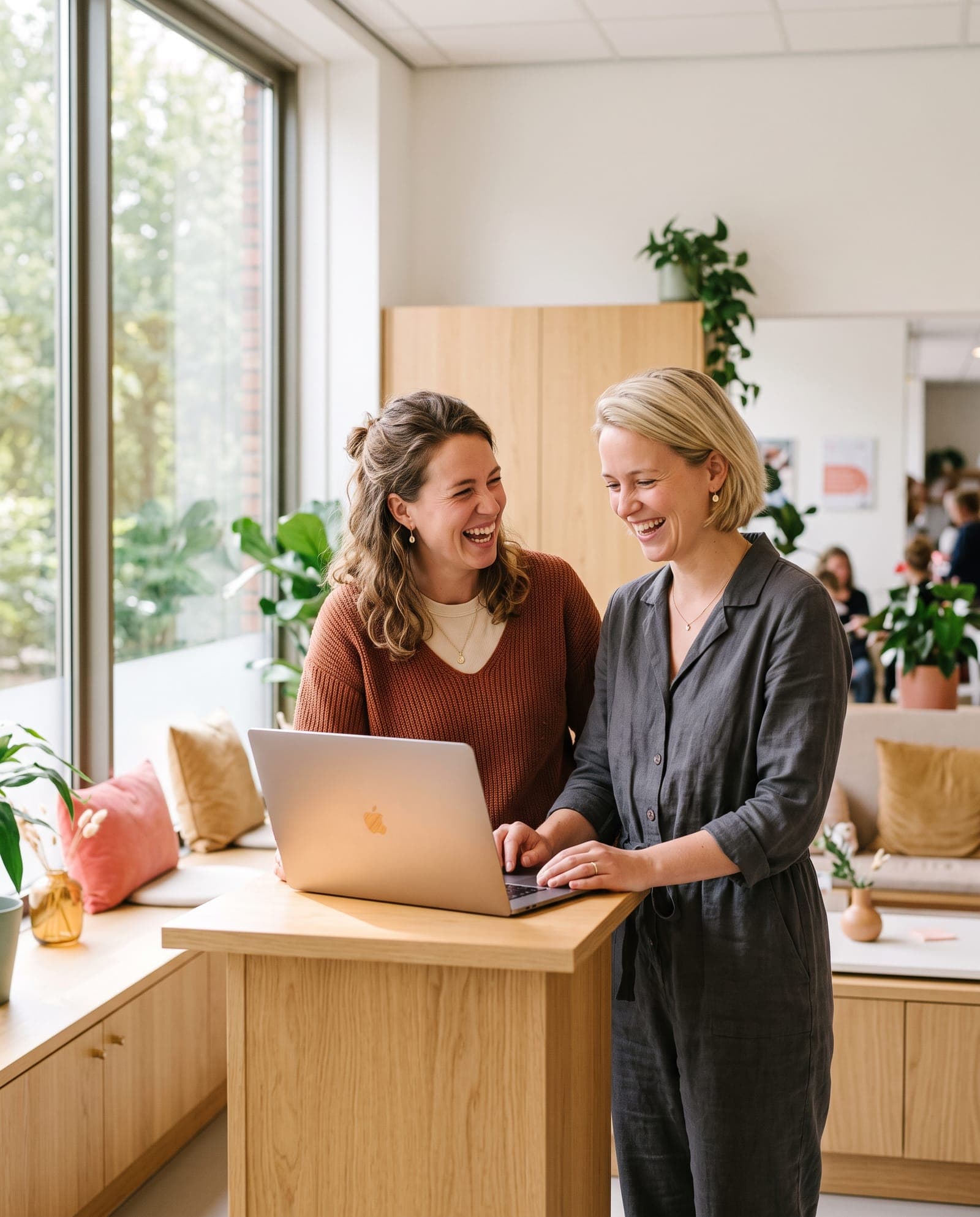 Twee collega's uit een verloskundigenpraktijk overleggen lachend achter een laptop